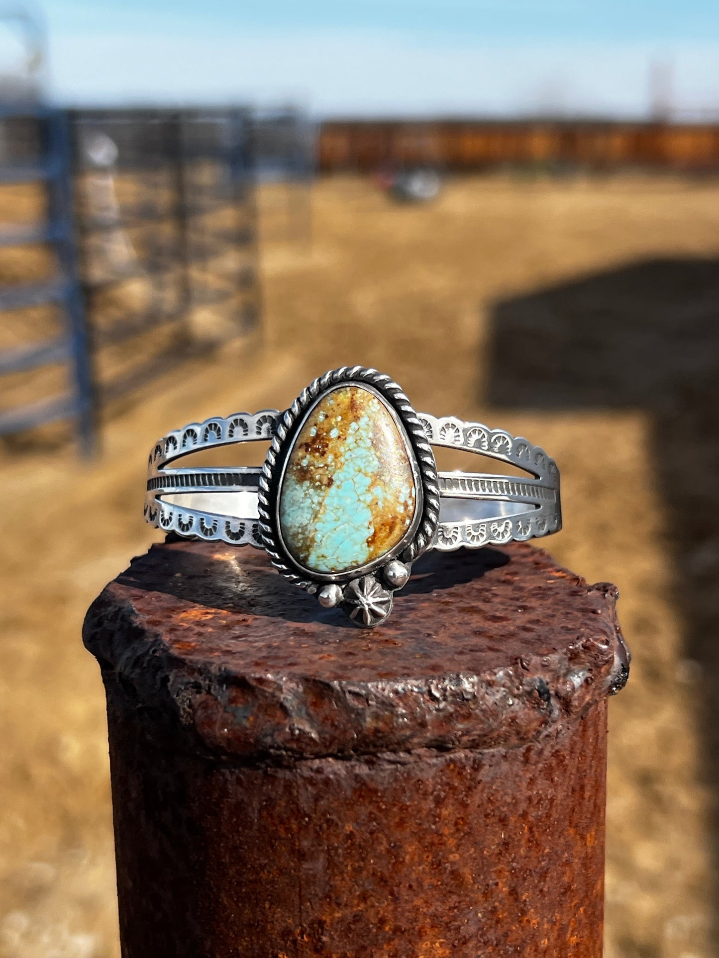 Silver bracelet with a turquoise stone on a rusted metal post outdoors.
