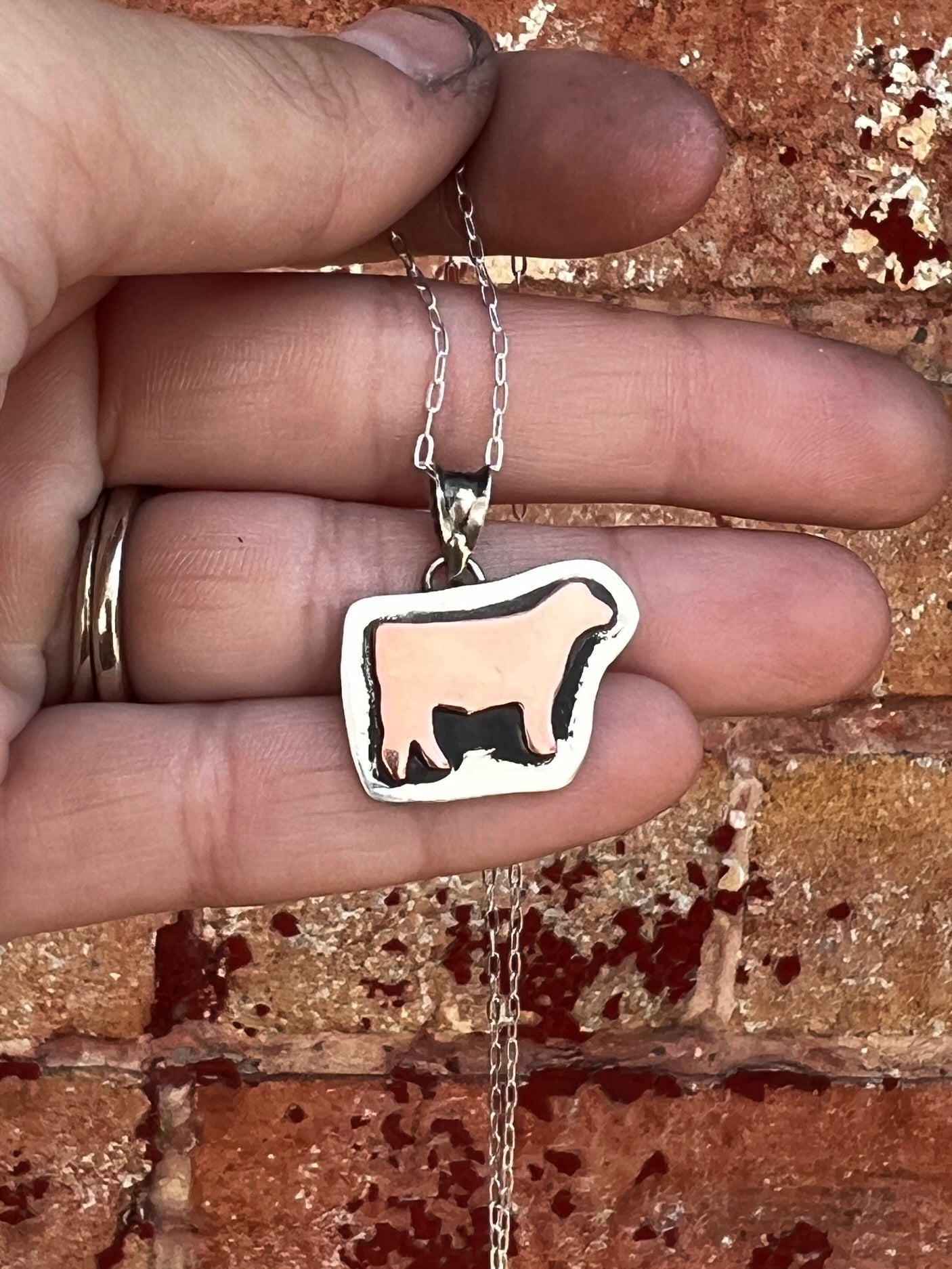 Hand holding a necklace with a cow-shaped pendant against a textured surface