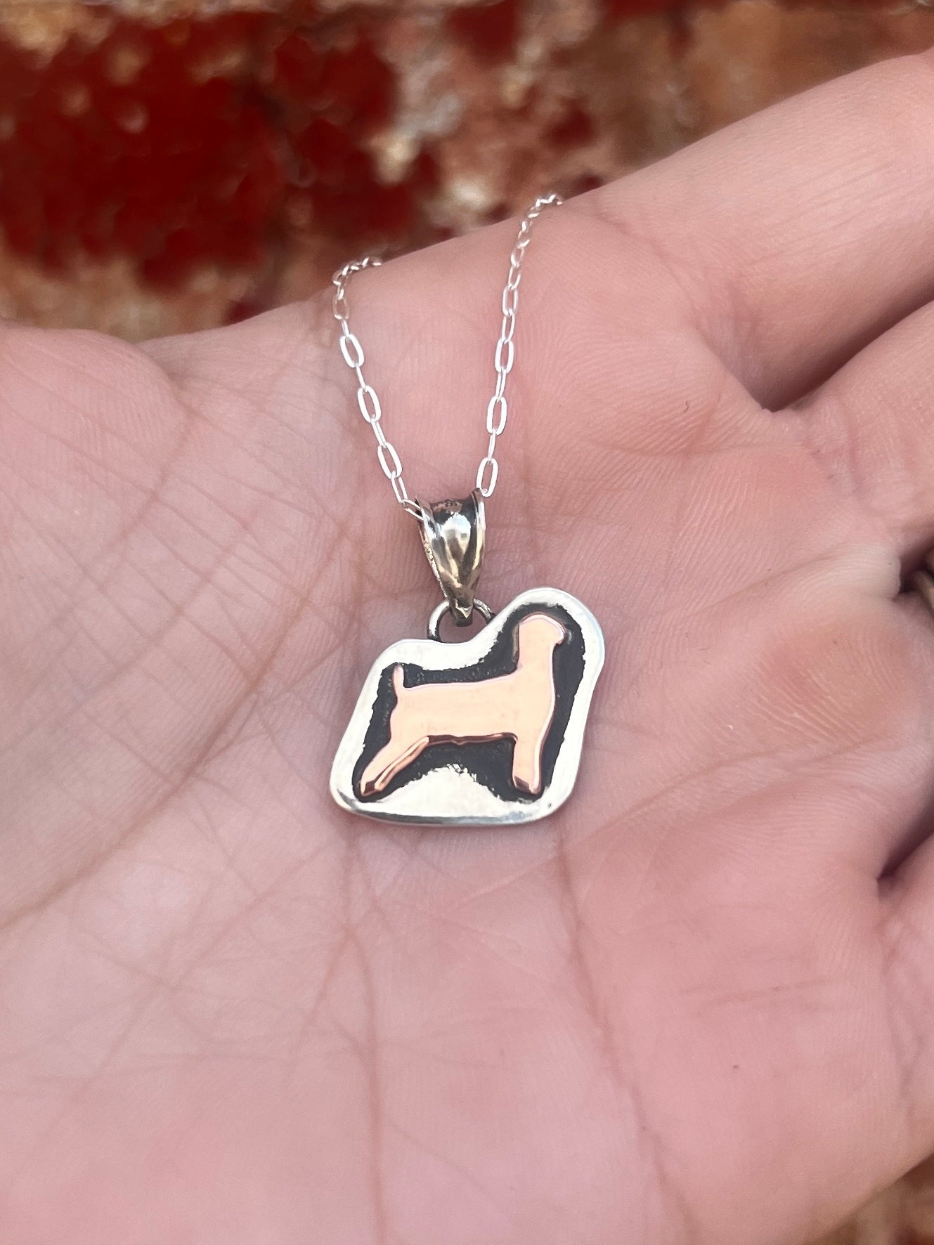Show goat shaped pendant on a chain held in a hand with a blurred background