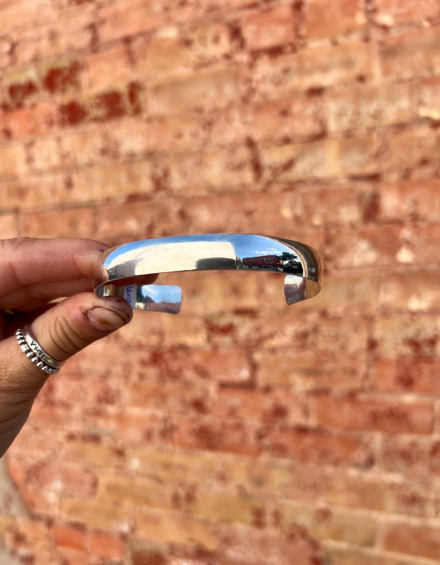 Metallic bracelet held by a hand against a brick wall background