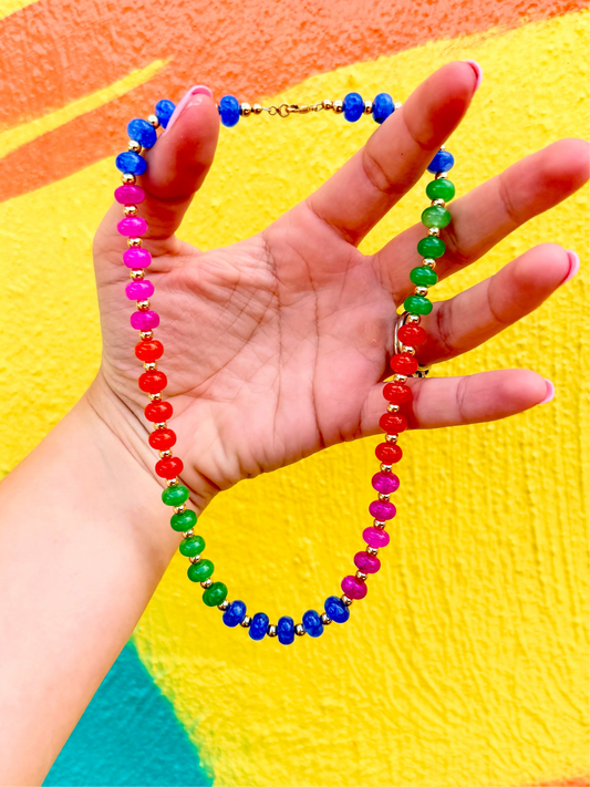 Colorful beaded necklace held by a hand against a multicolored background