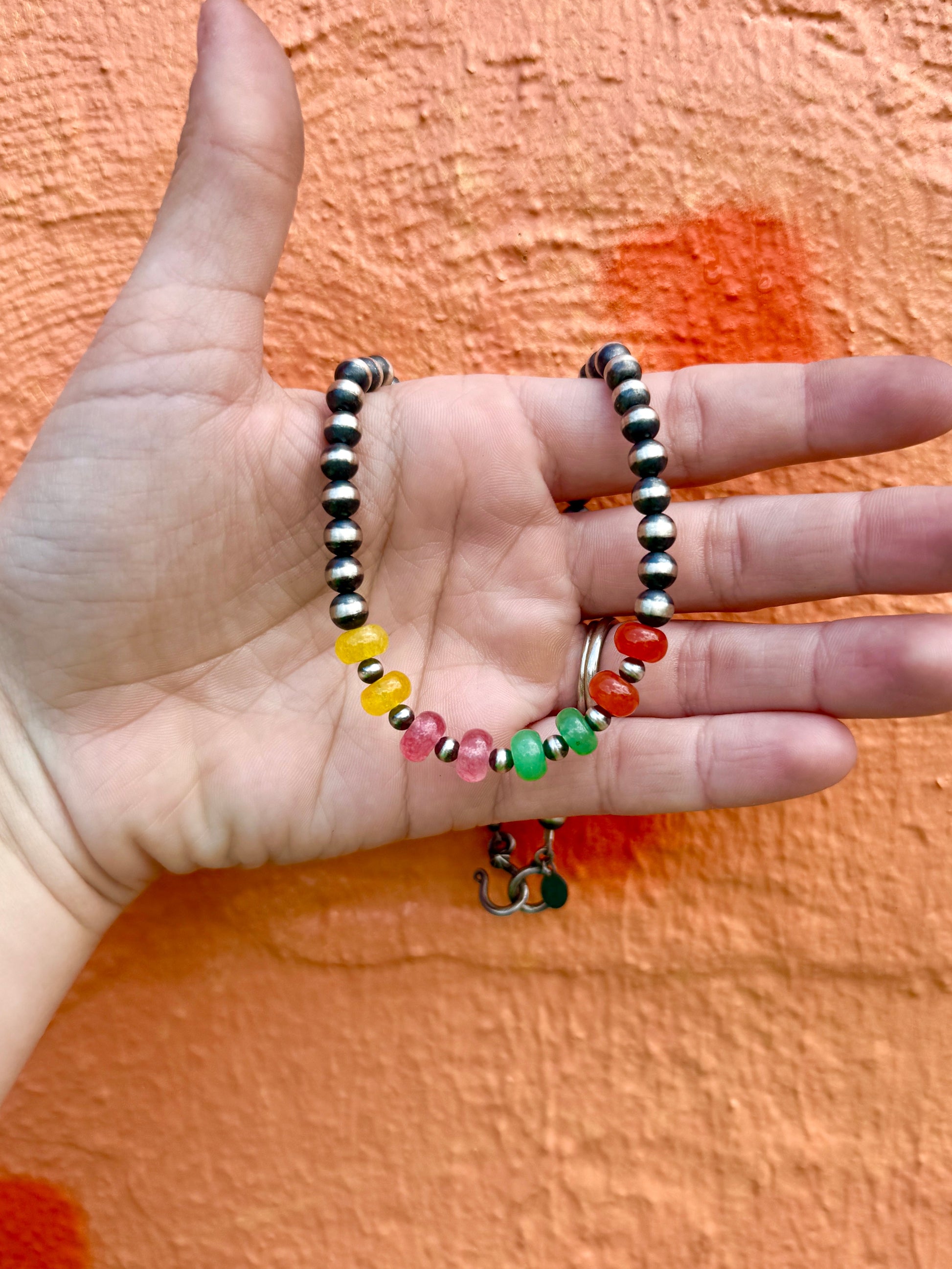 Hand holding a colorful beaded necklace against an orange background