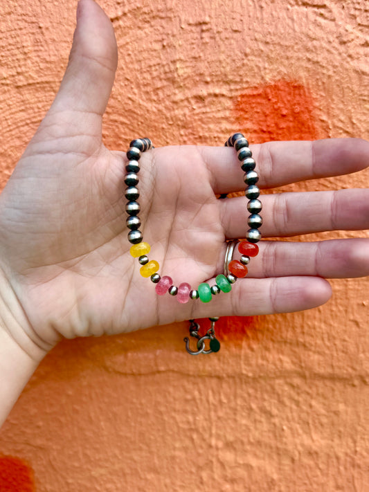 Hand holding a colorful beaded necklace against an orange background