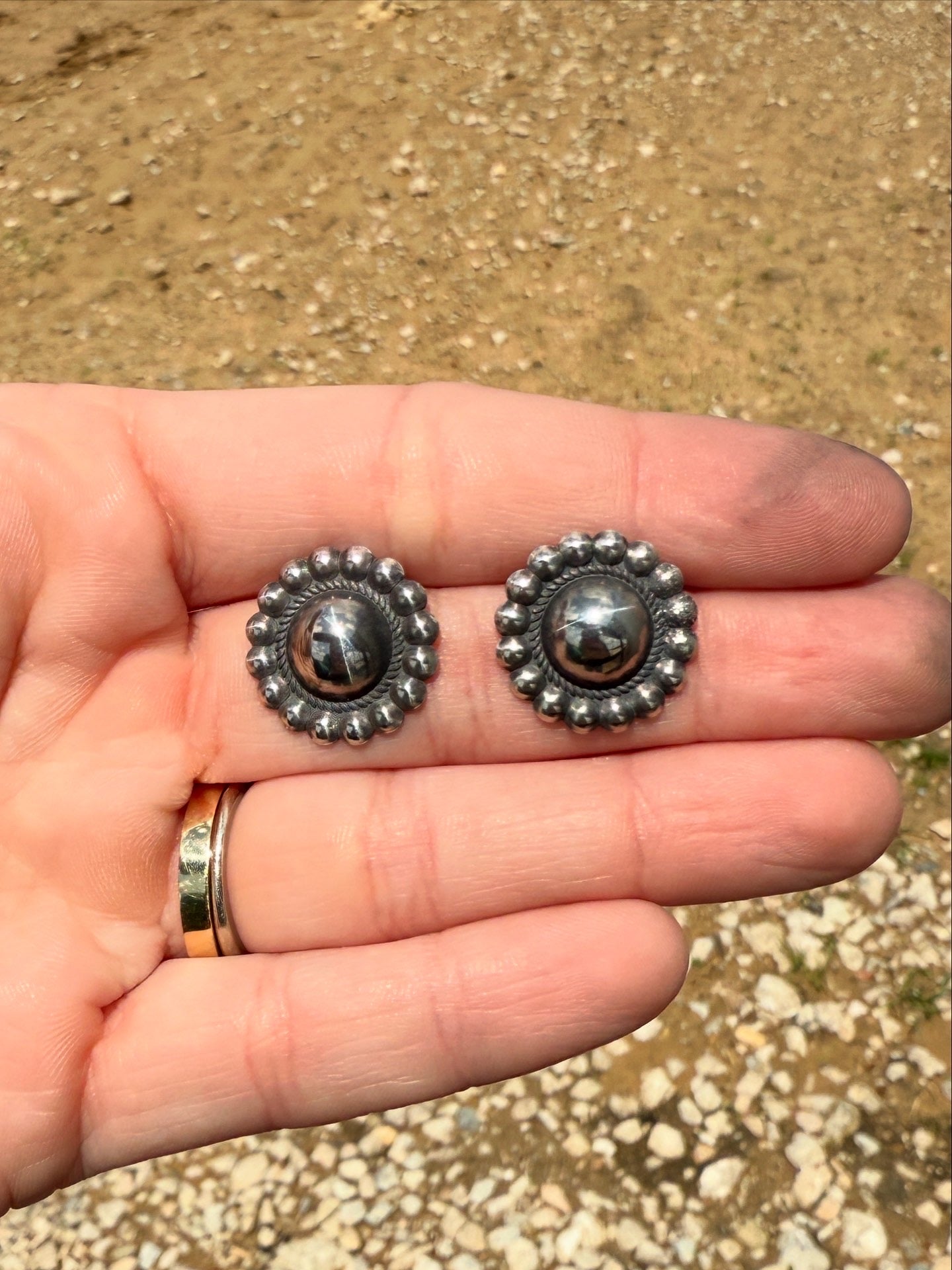 Silver beaded concho earrings held in a hand with a natural background