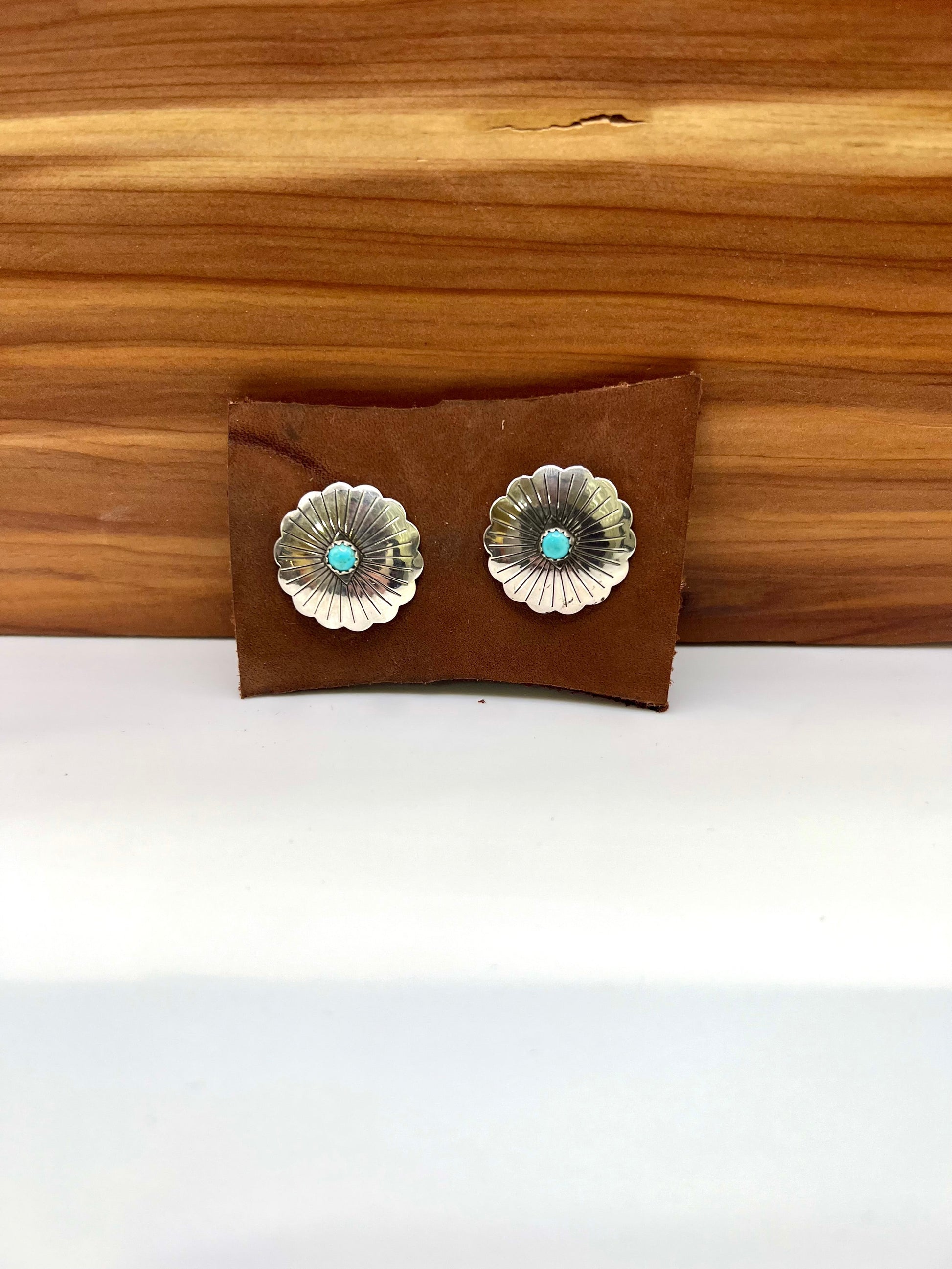 Floral silver earrings with turquoise stones on a brown leather pouch against a wooden background