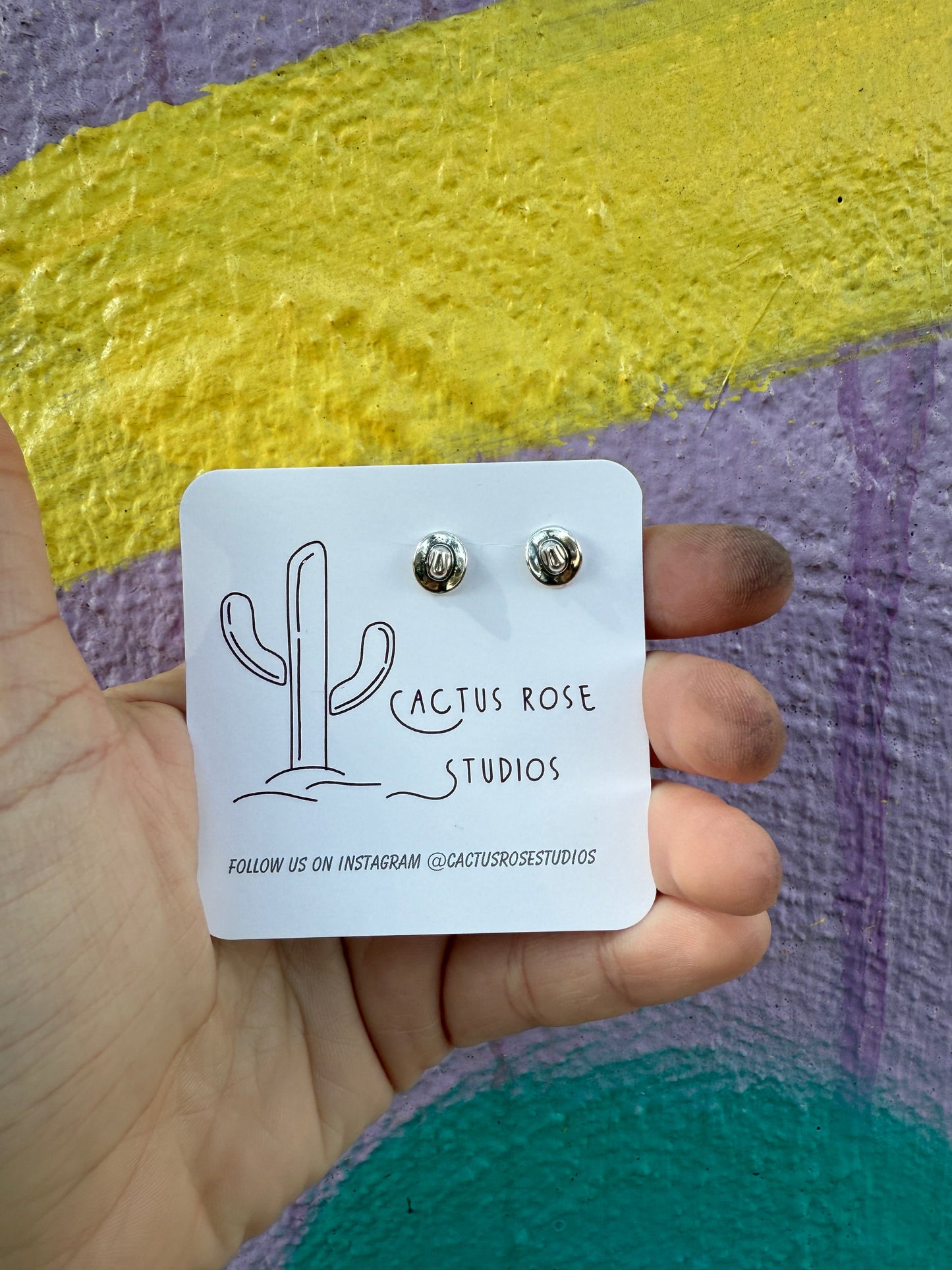 small cowboy hat shaped earrings aganst a colorful background