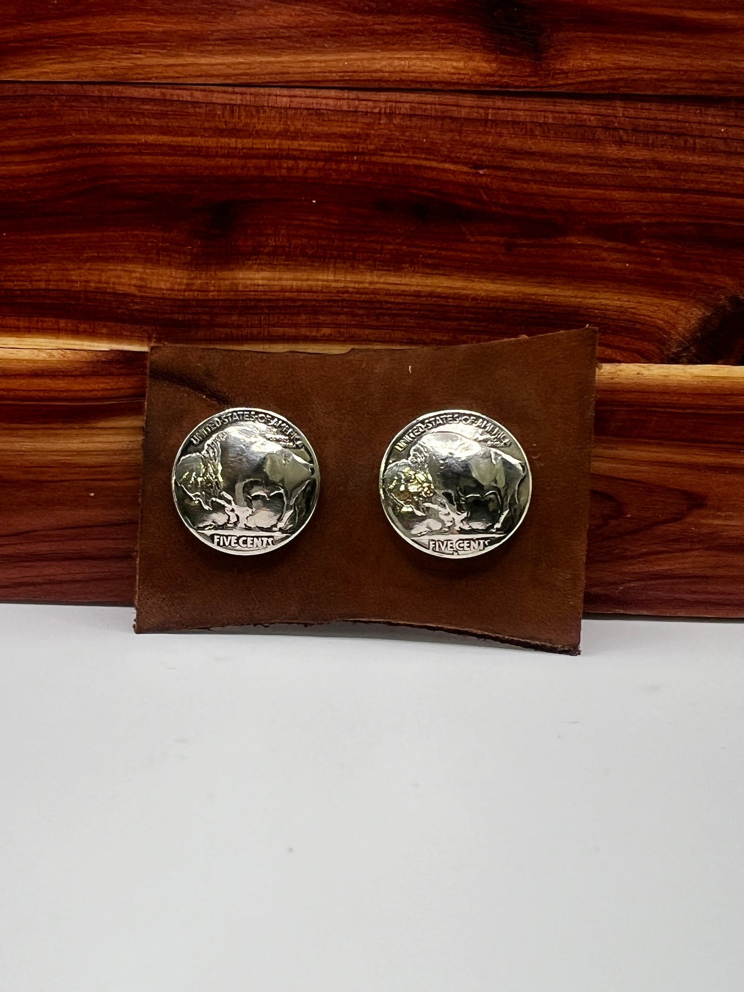 Silver coin earrings on a brown leather card with a wooden background