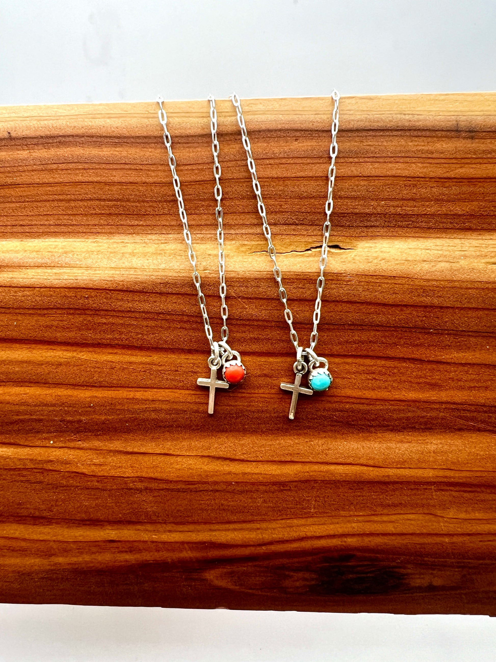 Two silver necklaces with cross charms on a wooden surface