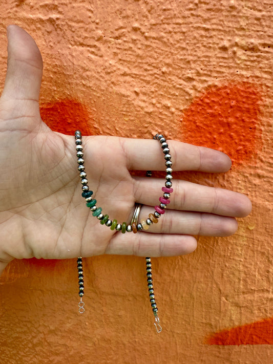 Hand holding beaded sterling silver pearl necklace against an orange background