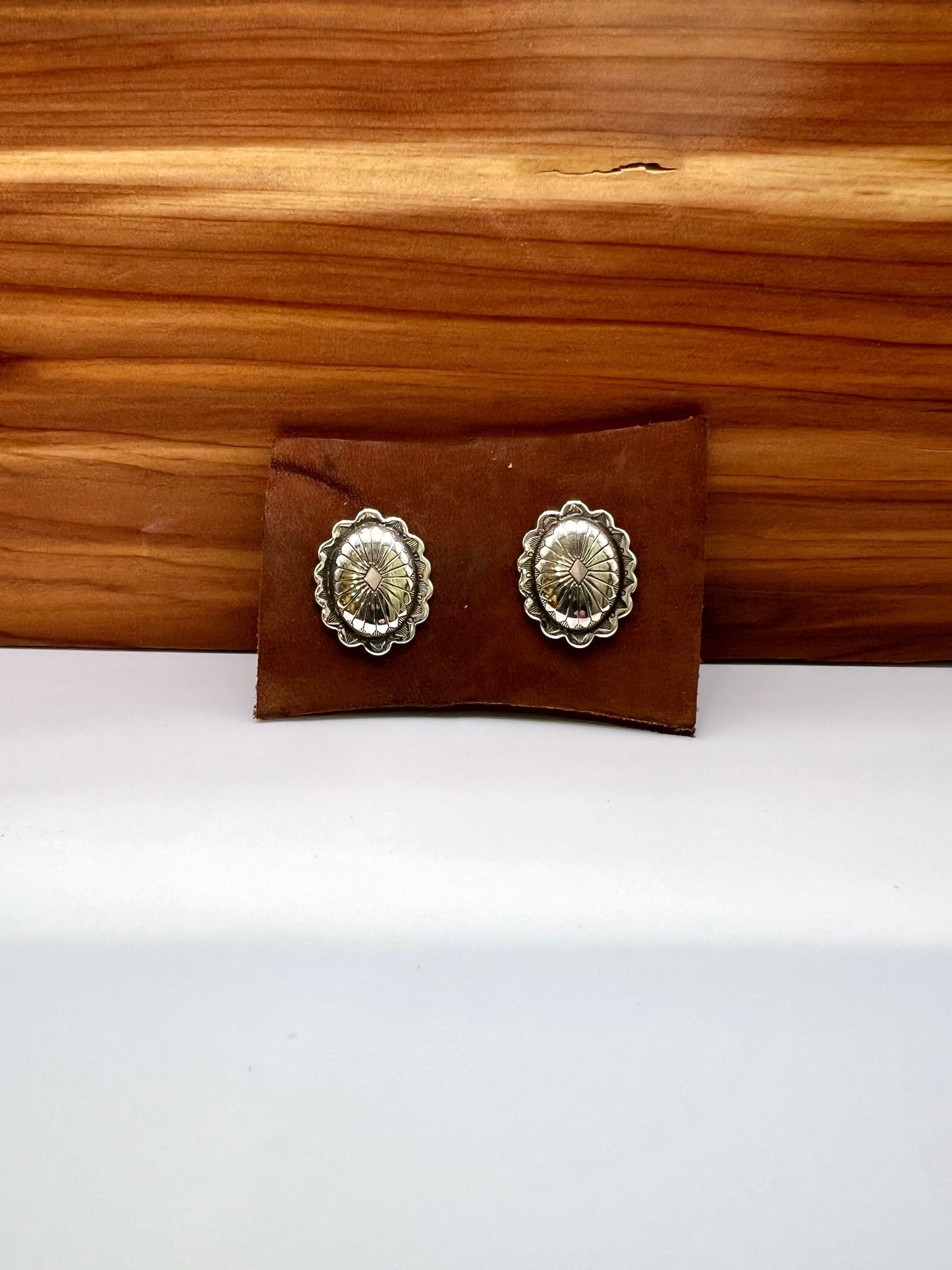 Pair of silver concho-style earrings on a brown leather case against a wooden background