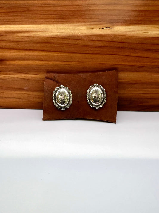 Pair of silver concho-style earrings on a brown leather case against a wooden background