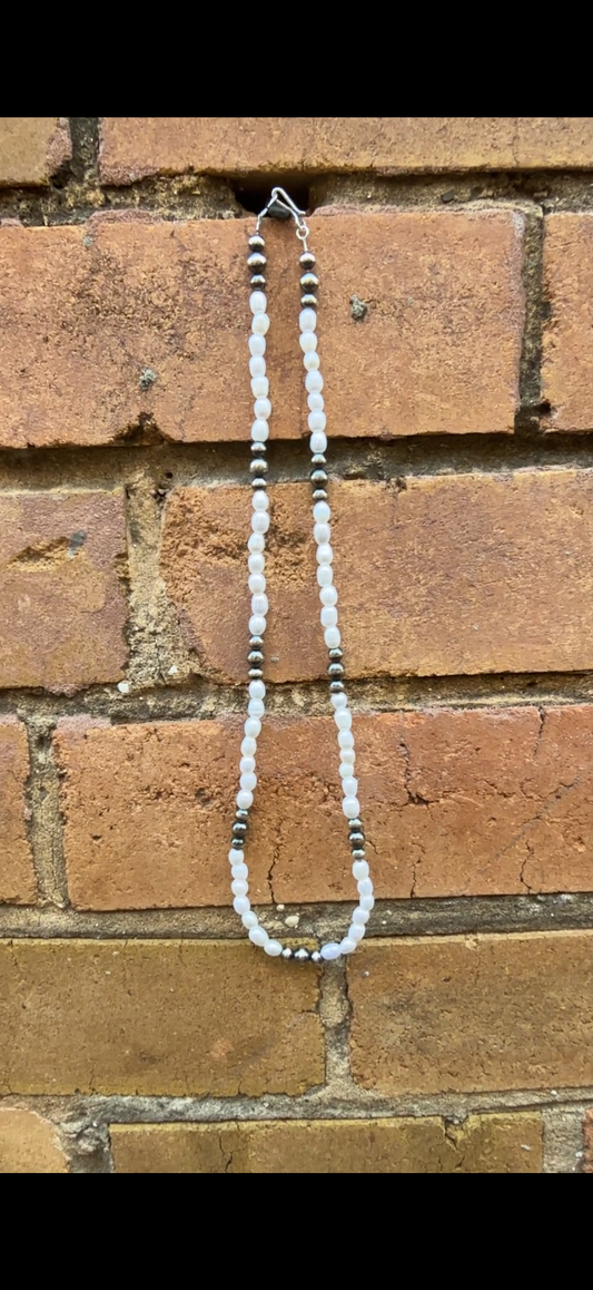 Necklace with sterling silver pearls and freshwater rice shaped pearls hanging against a brick wall.