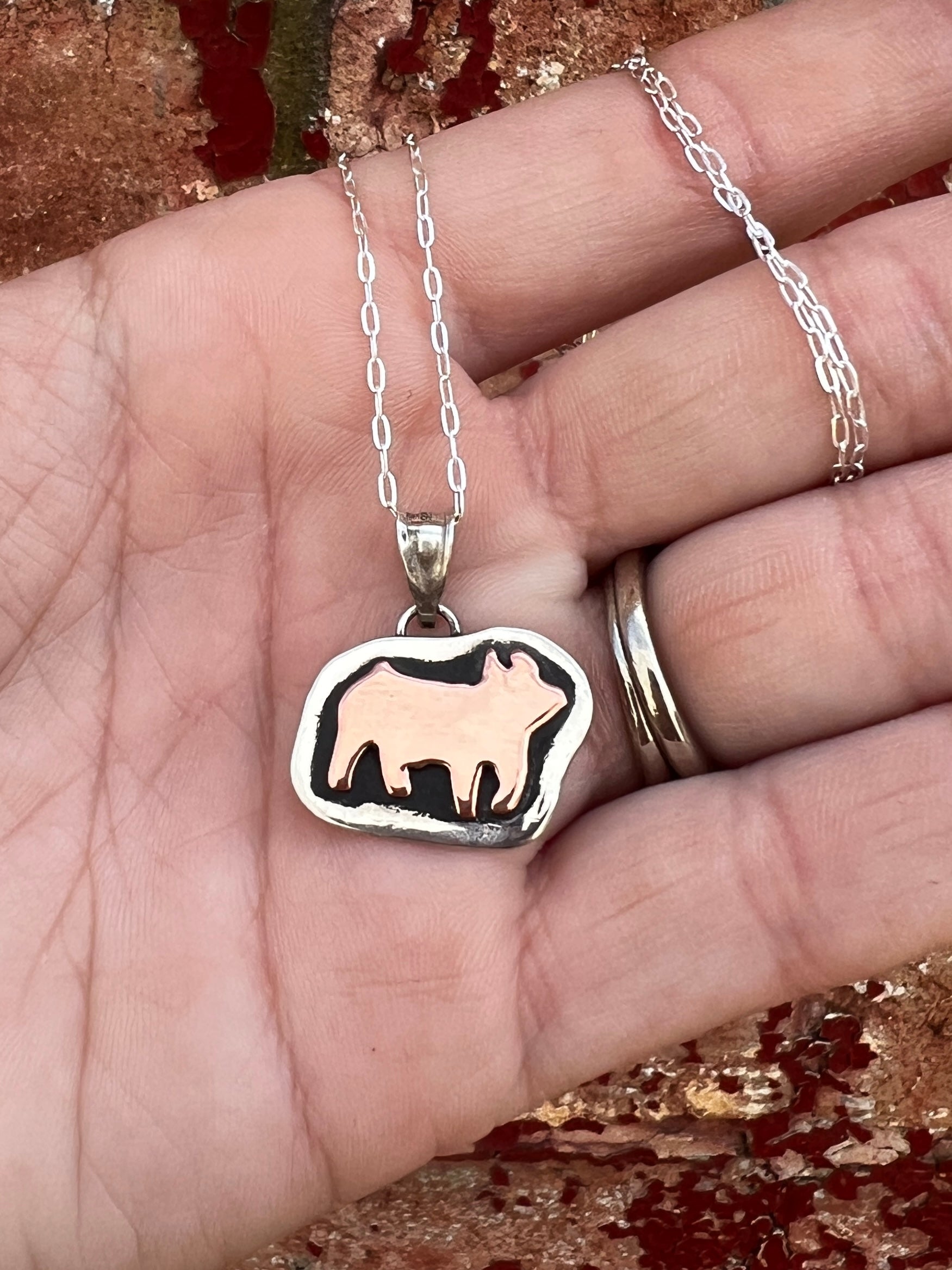 Silver necklace with a show pig (swine) pendant held in a hand against a textured background