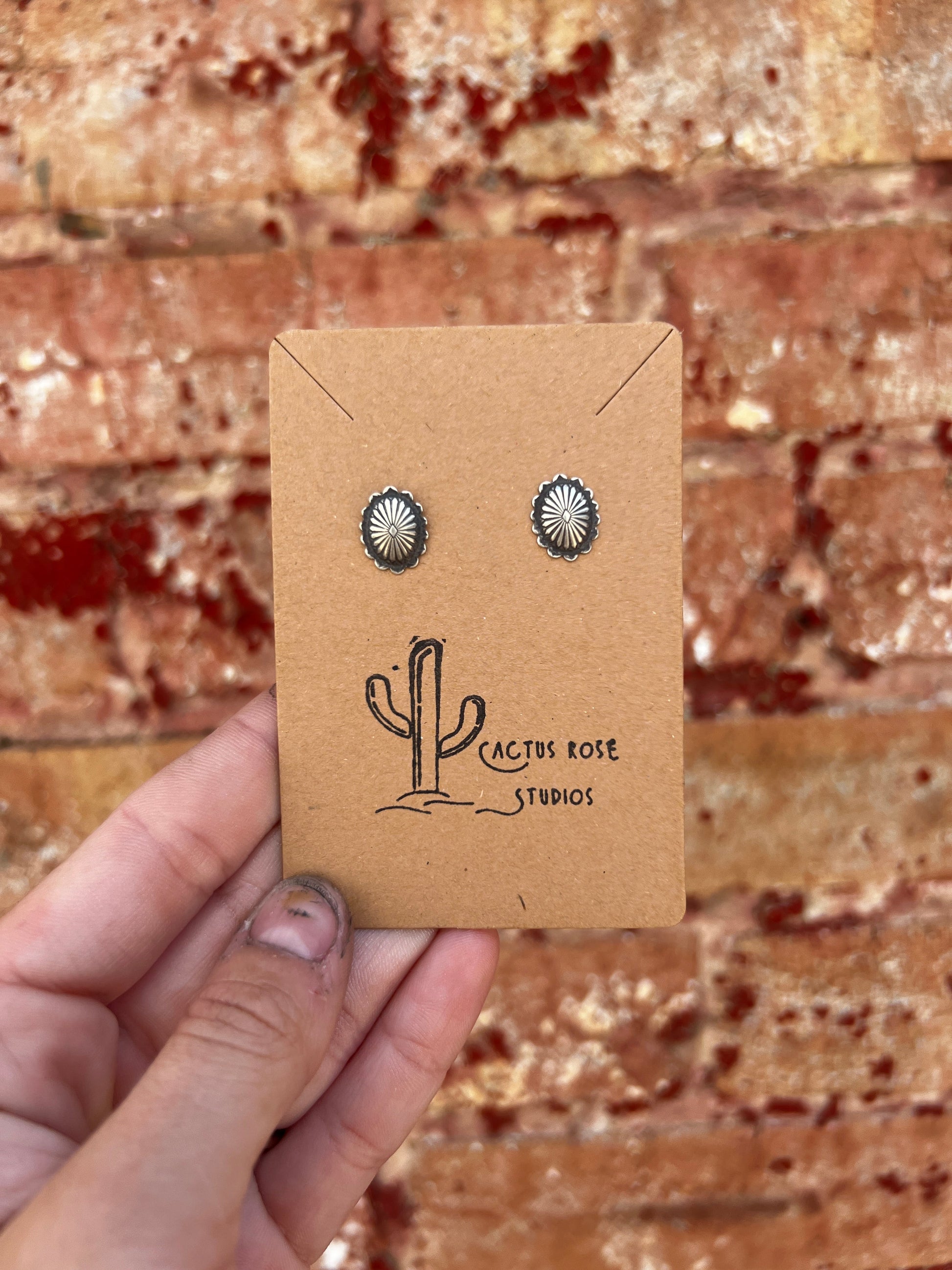sterling silver oval shaped  earrings on a branded card held against a brick wall.