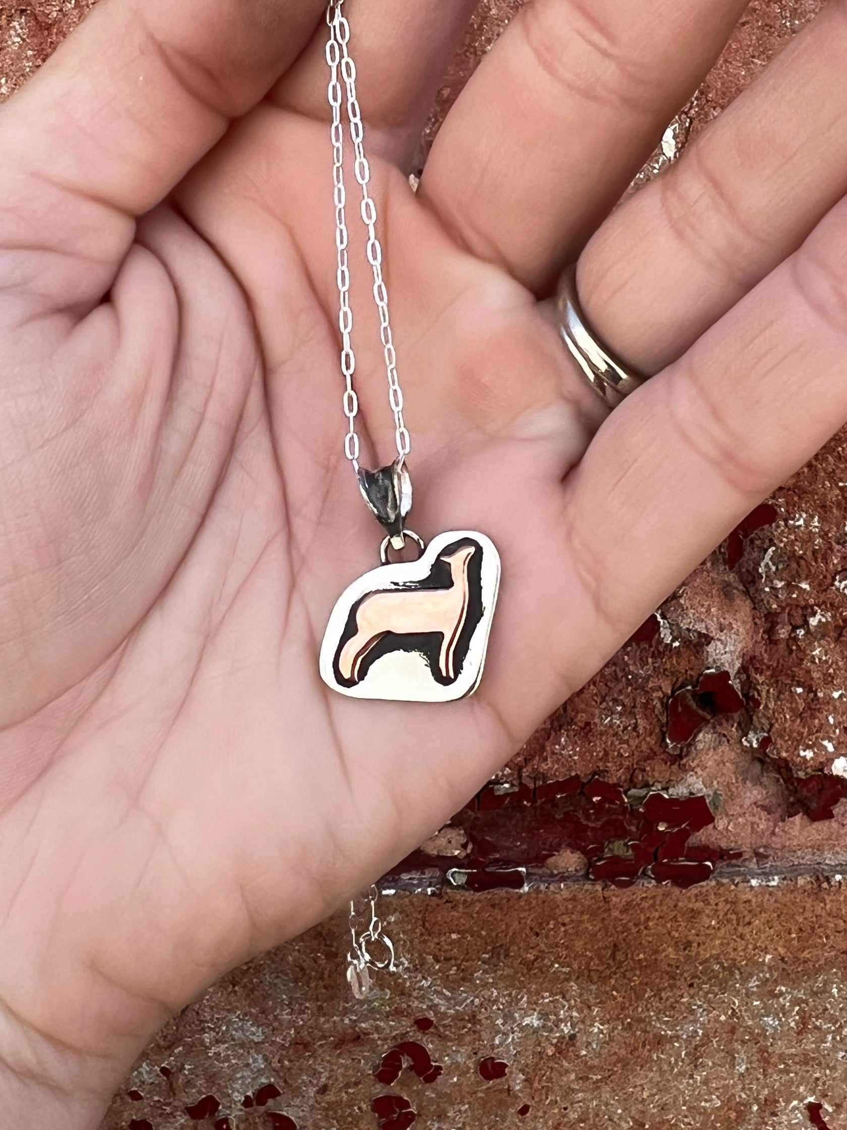 Silver pendant with a show sheep (lamb) design held in a hand against a textured background