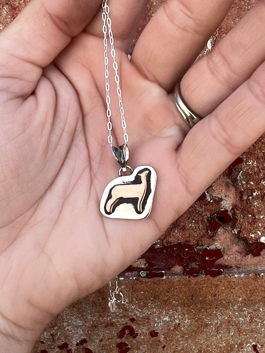 Silver pendant with a show sheep (lamb) design held in a hand against a textured background