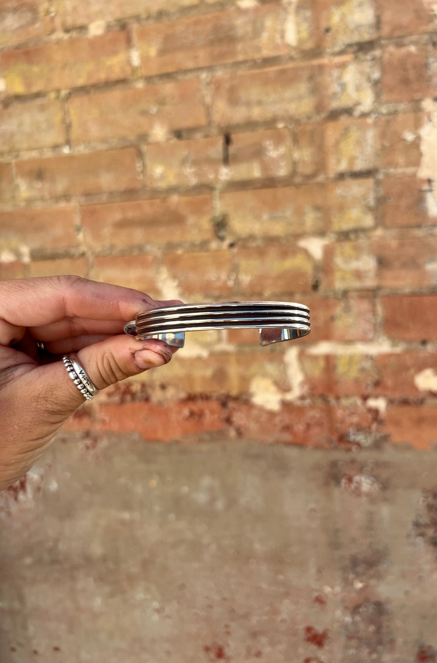 Hand holding a silver bracelet against a brick wall background