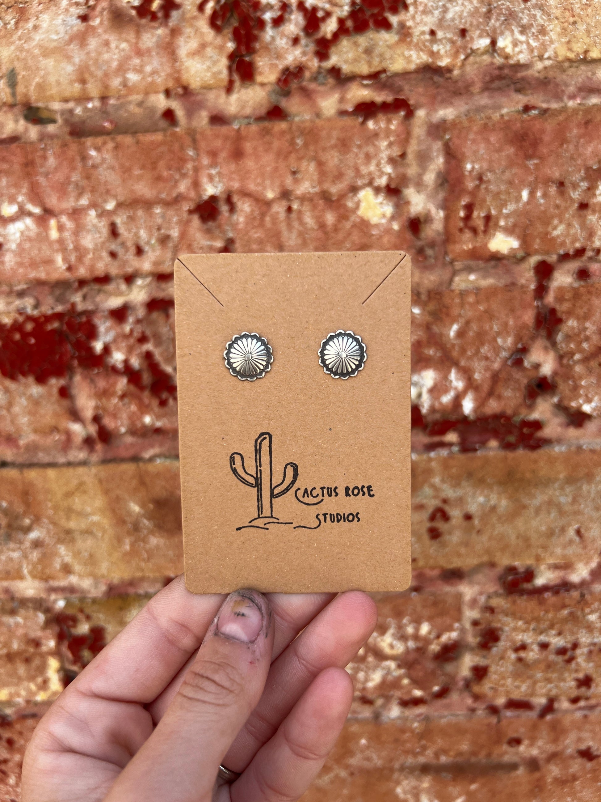 Pair of silver earrings on a Cactus Rose Studios card held against a brick wall.