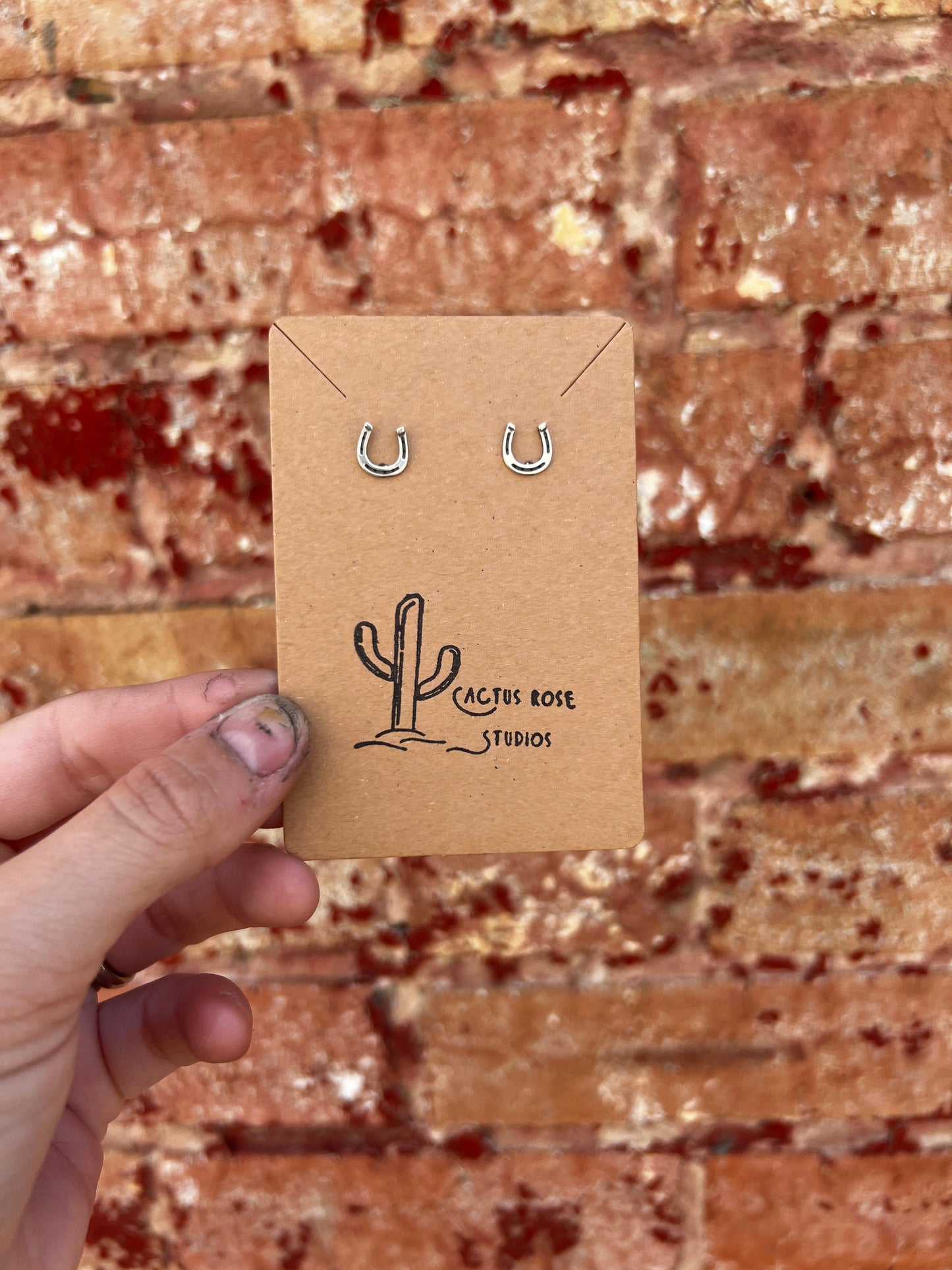Horseshoe earrings on a Cactus Rose Studios card against a brick wall background
