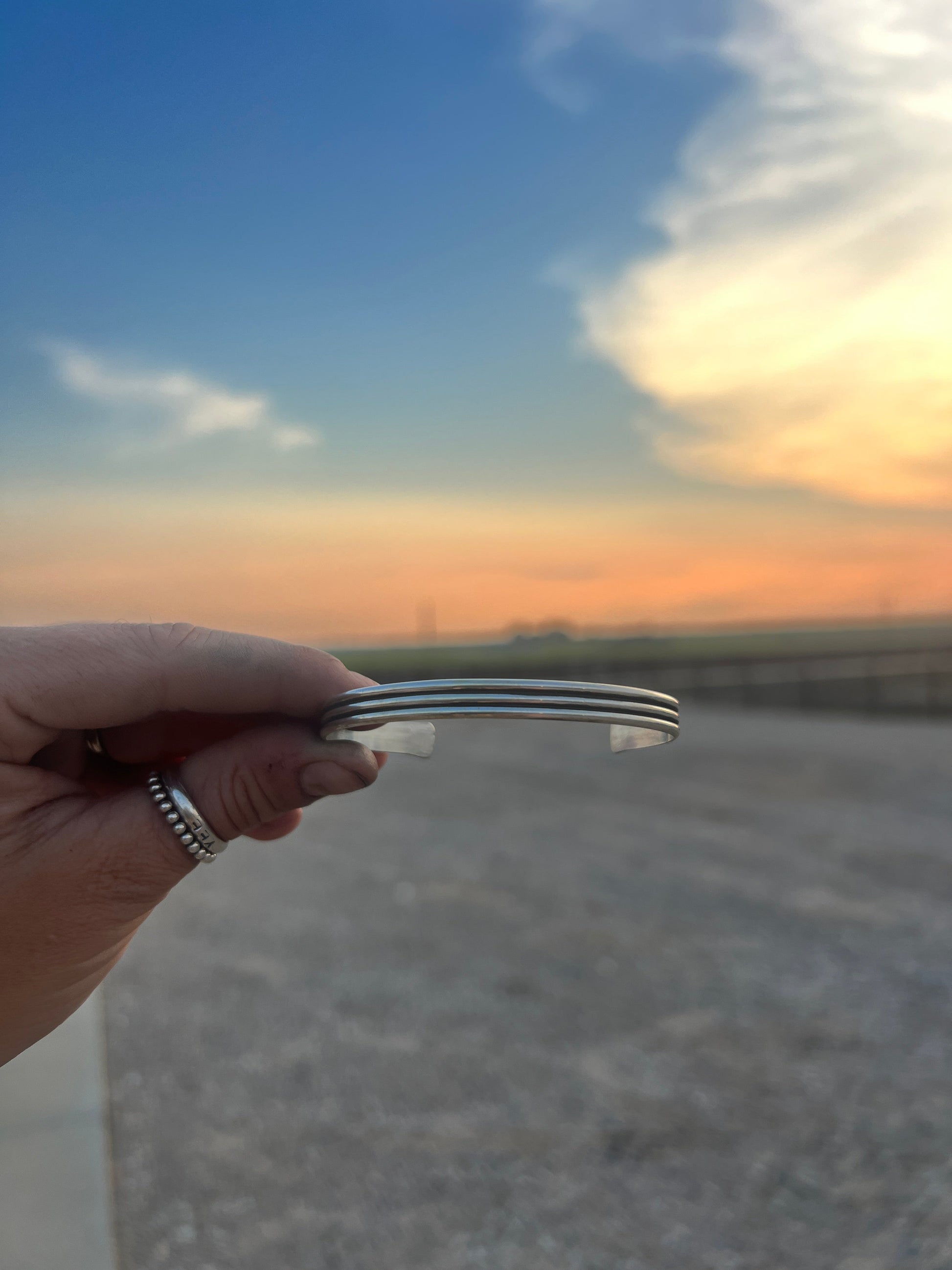 Hand holding a metallic object with a sunset or sunrise sky in the background