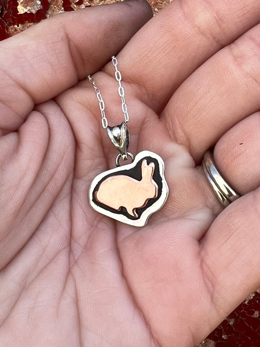 Hand holding a necklace with a  pendant featuring a rabbit design.
